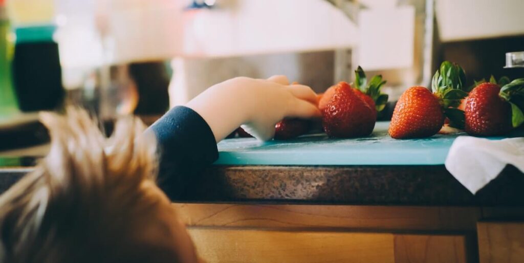 Bambino che prende delle fragole da un piano di lavoro